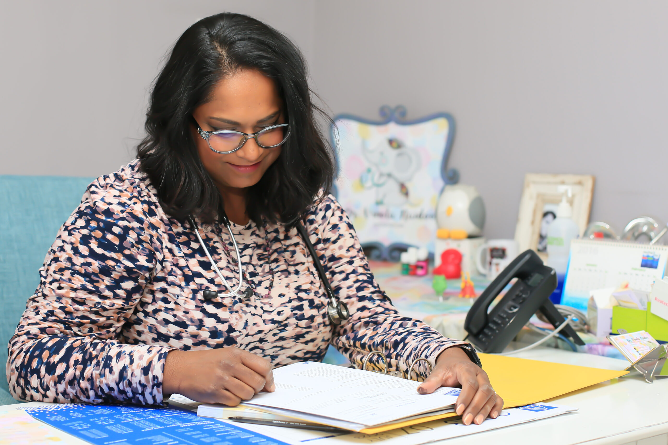 Dr. Vinola Naidoo reviewing medical notes at her desk, focused and calm, in a bright, welcoming pediatric office.